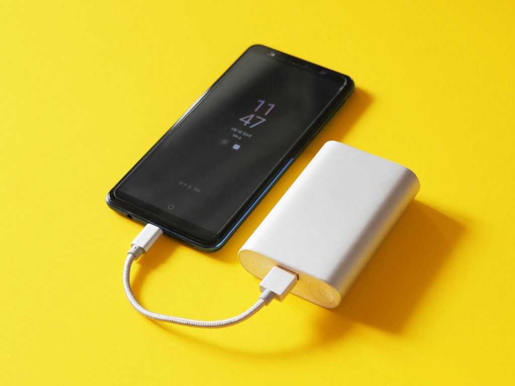 smartphone branché à une batterie externe grâce à un câble court sur un fond jaune